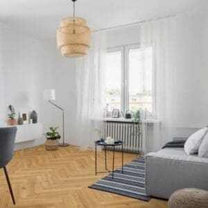 Modern living room with natural oak herringbone flooring featuring grey sofa and woven pendant light