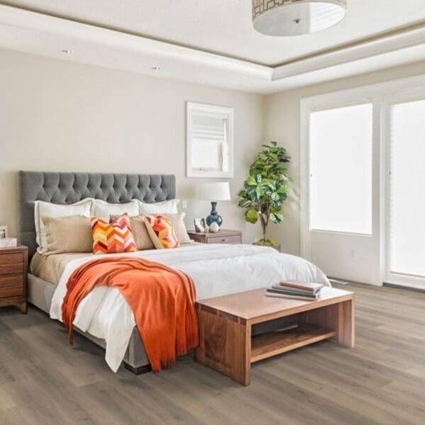 Greige oak laminate flooring in bedroom with grey headboard and wooden furniture