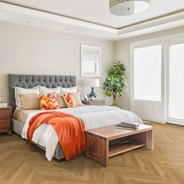 Bedroom with grey headboard and oak herringbone flooring with wooden furniture