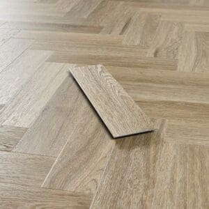 Angled perspective of Smoky Oak herringbone flooring with a single loose plank showing thickness.