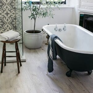 Cove wood effect flooring in a bathroom featuring a black roll top bath