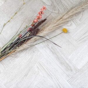 Top down view of White Oak Parquet laid in a herringbone pattern with decorative dried flowers