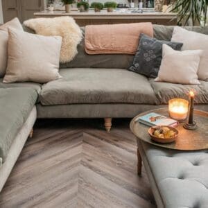 Lounge area showing the geometric pattern of chevron flooring under a grey velvet sofa.