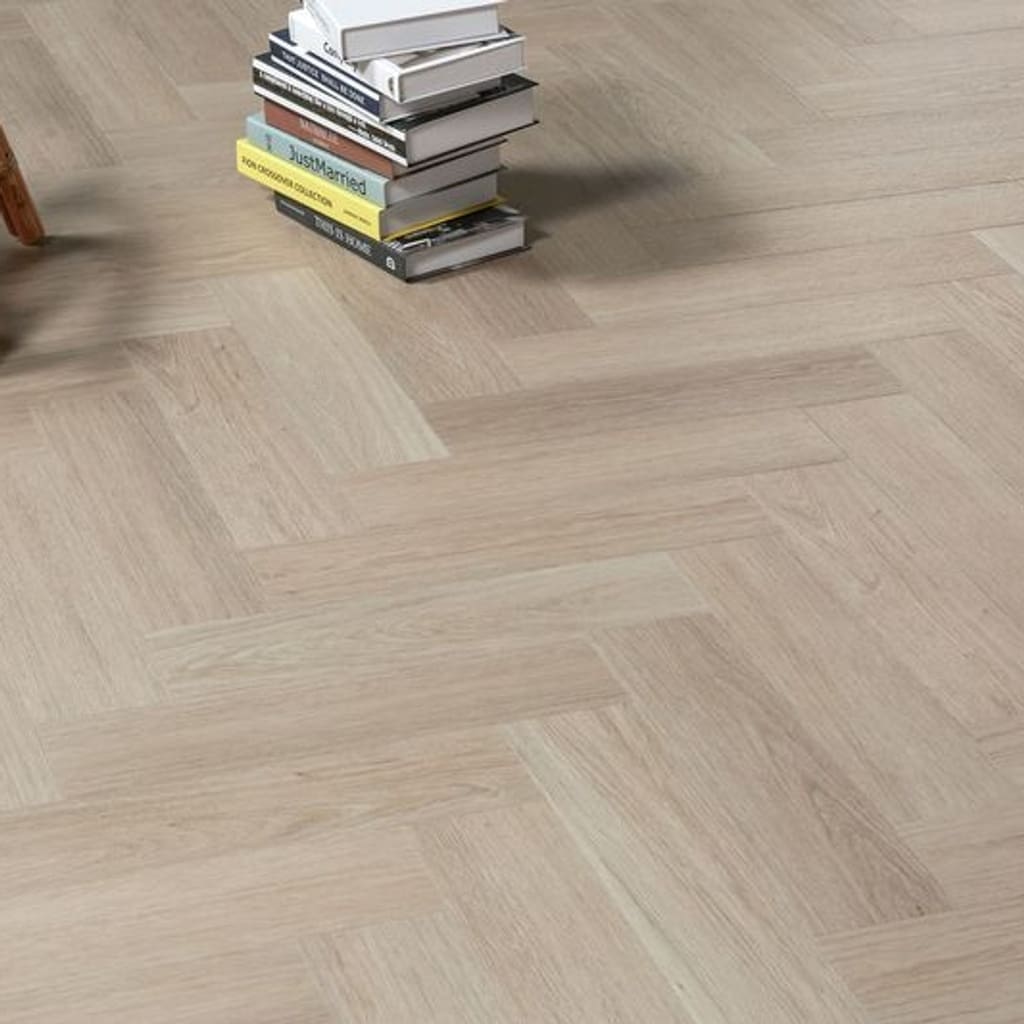 Vermont Ash herringbone flooring in a room with a stack of books and a wicker chair.